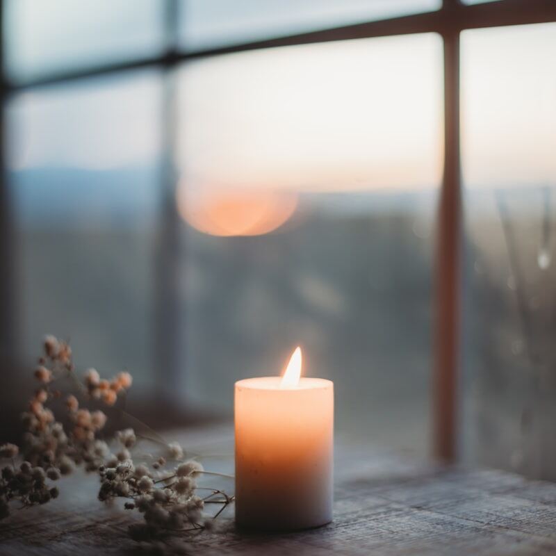 Pencere kenarında yanan bir mum ve kurutulmuş çiçekler